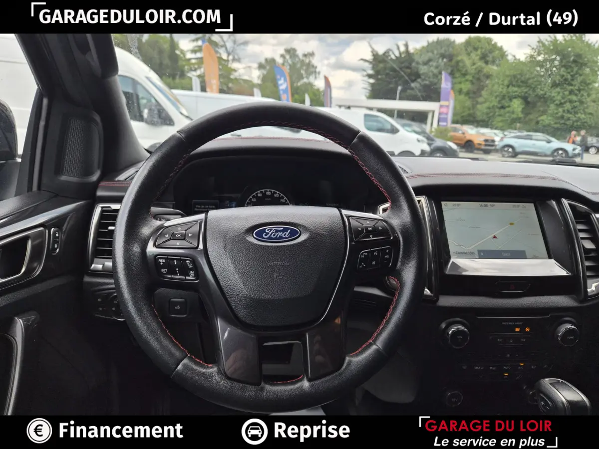Vue intérieure centrée sur le volant cuir noir avec coutures rouges du Ford Ranger gris foncé, écran tactile et tableau de bord visibles.