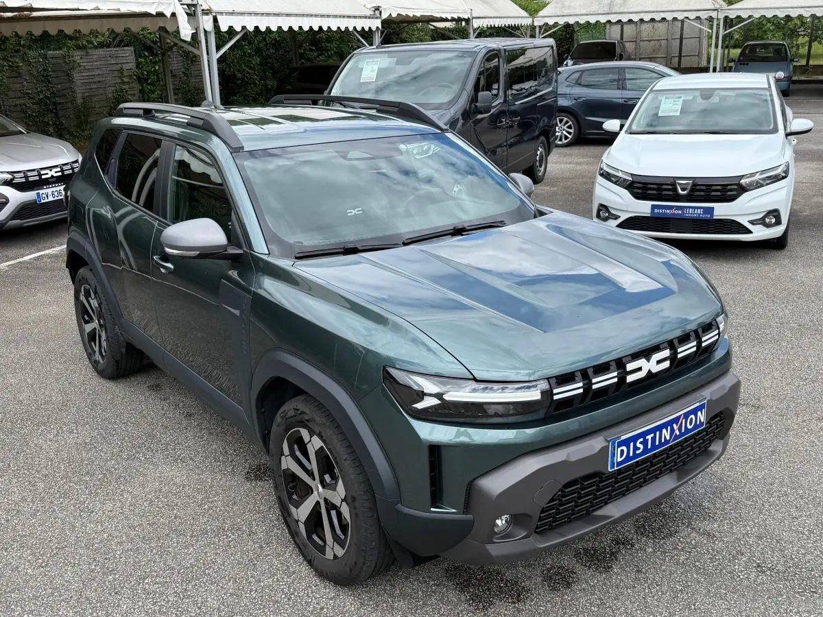 Vue 3/4 avant d’un Dacia Duster Hybrid 140 Journey vert cèdre avec calandre noire et jantes bicolores sur parking.