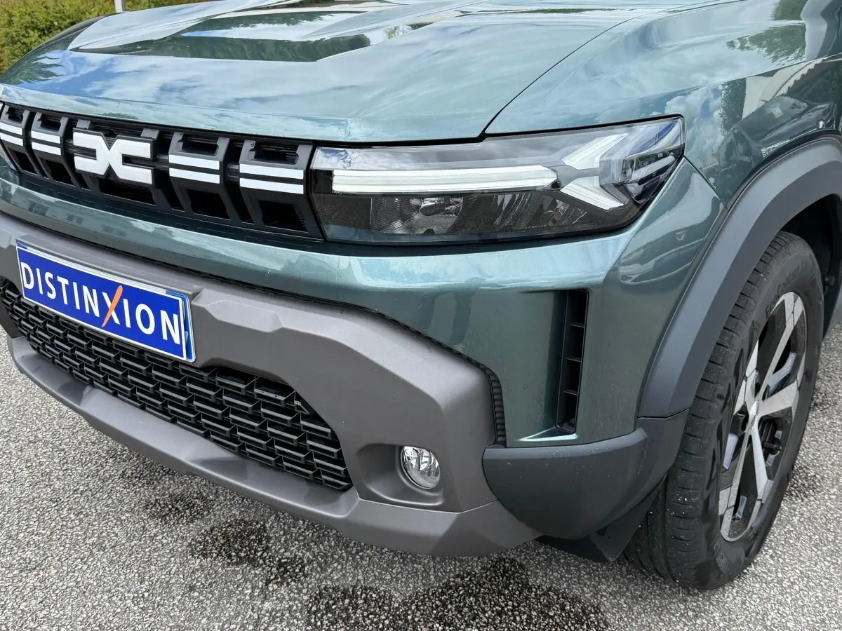 Gros plan sur l’avant droit du Dacia Duster Hybrid 140 Journey vert cèdre, mettant en valeur la calandre et les phares LED.