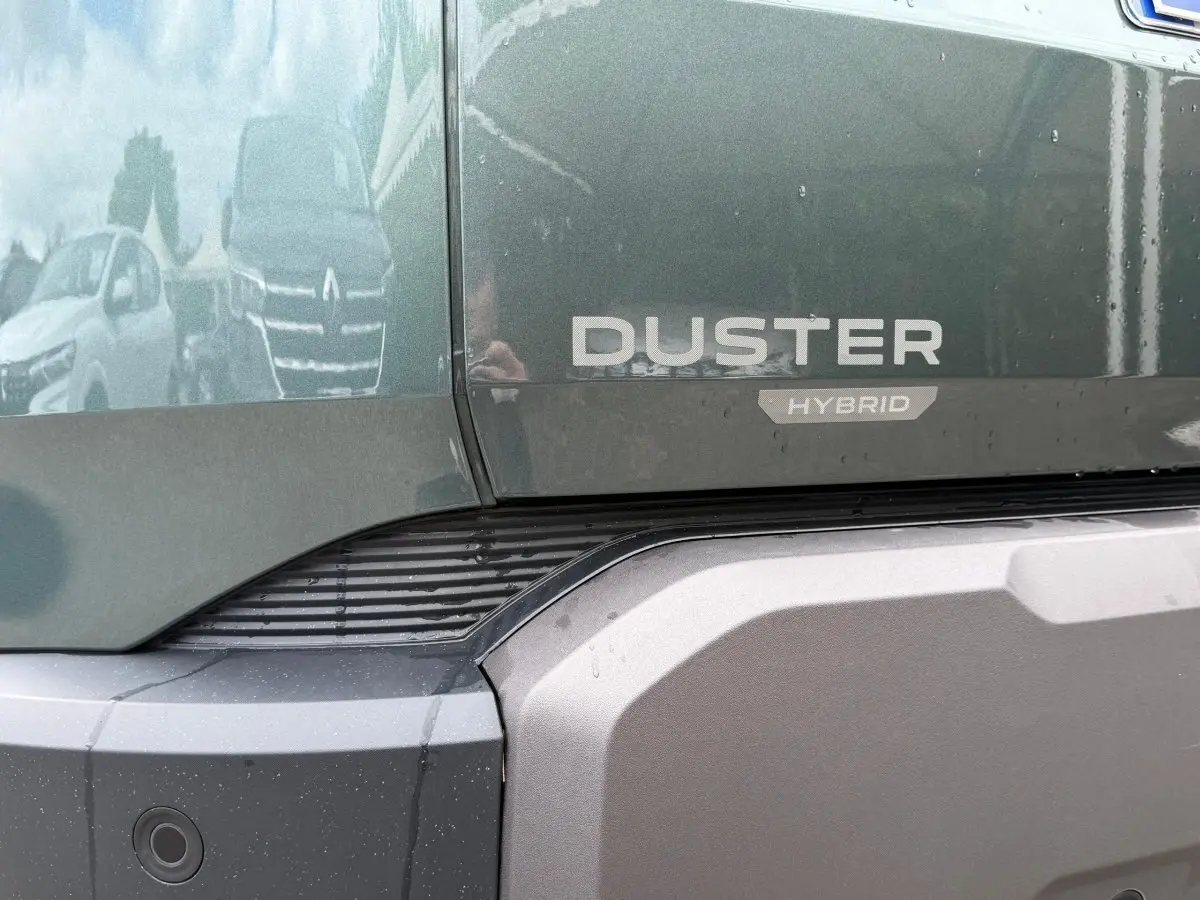 Gros plan sur l'arrière vert cèdre du Dacia Duster Hybrid avec logo et pare-chocs gris texturé.