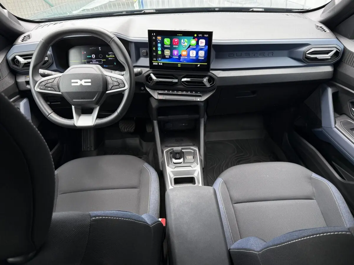 Vue intérieure avant du Dacia Duster Hybrid 140 Journey 2025, tableau de bord moderne avec écran tactile central et volant multifonctions.