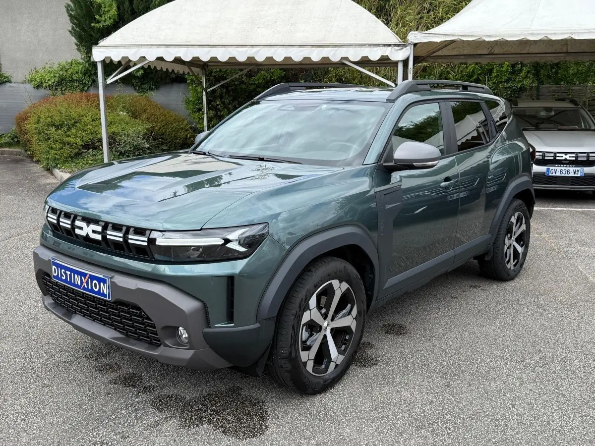 Dacia Duster Hybrid 140 Journey vert cèdre en 3/4 avant droit, avec jantes alliage et barres de toit noires.
