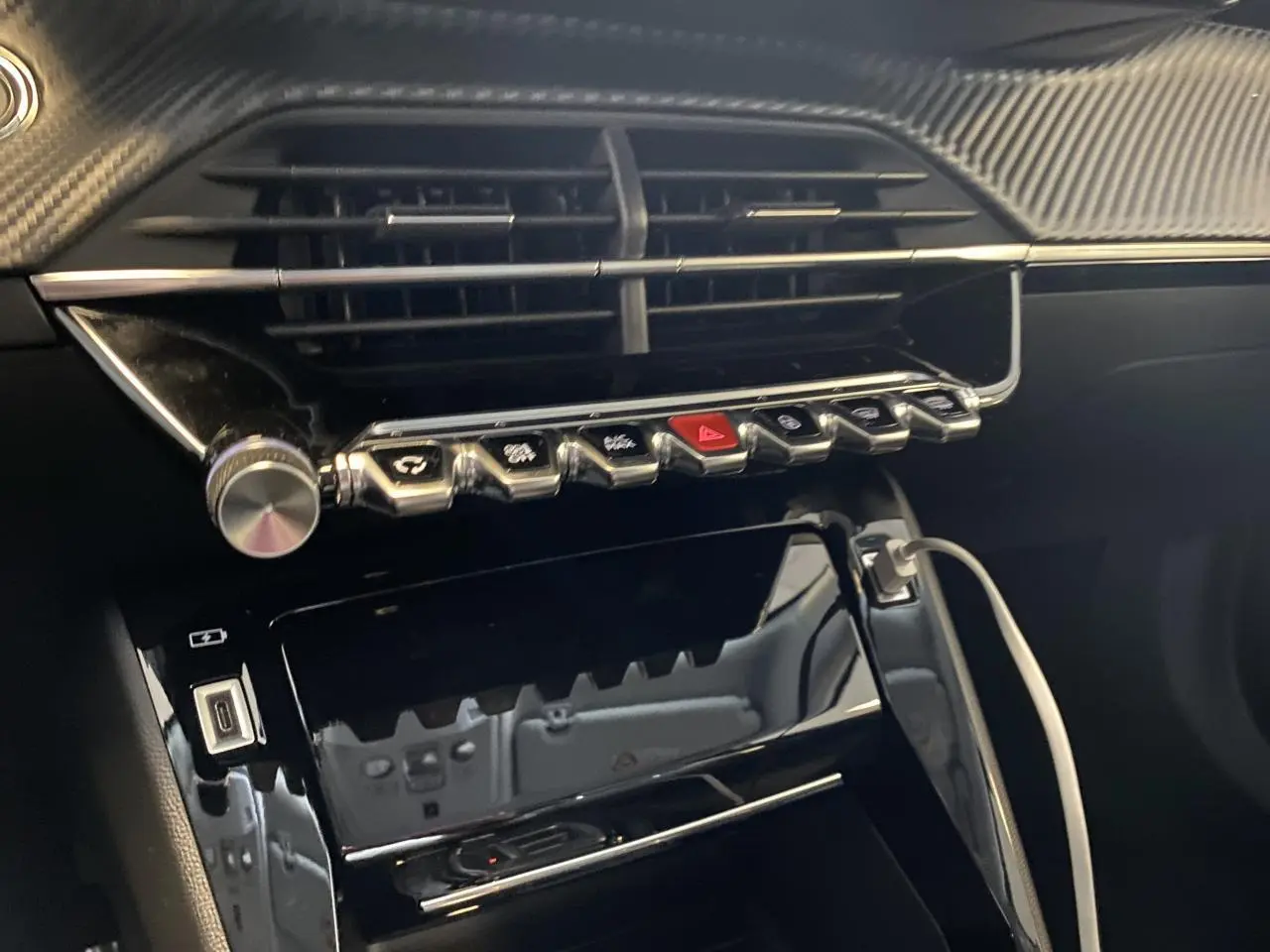 Vue rapprochée de la console centrale noire brillante du Peugeot 2008 e-136 Allure Pack avec boutons chromés et câble USB connecté.