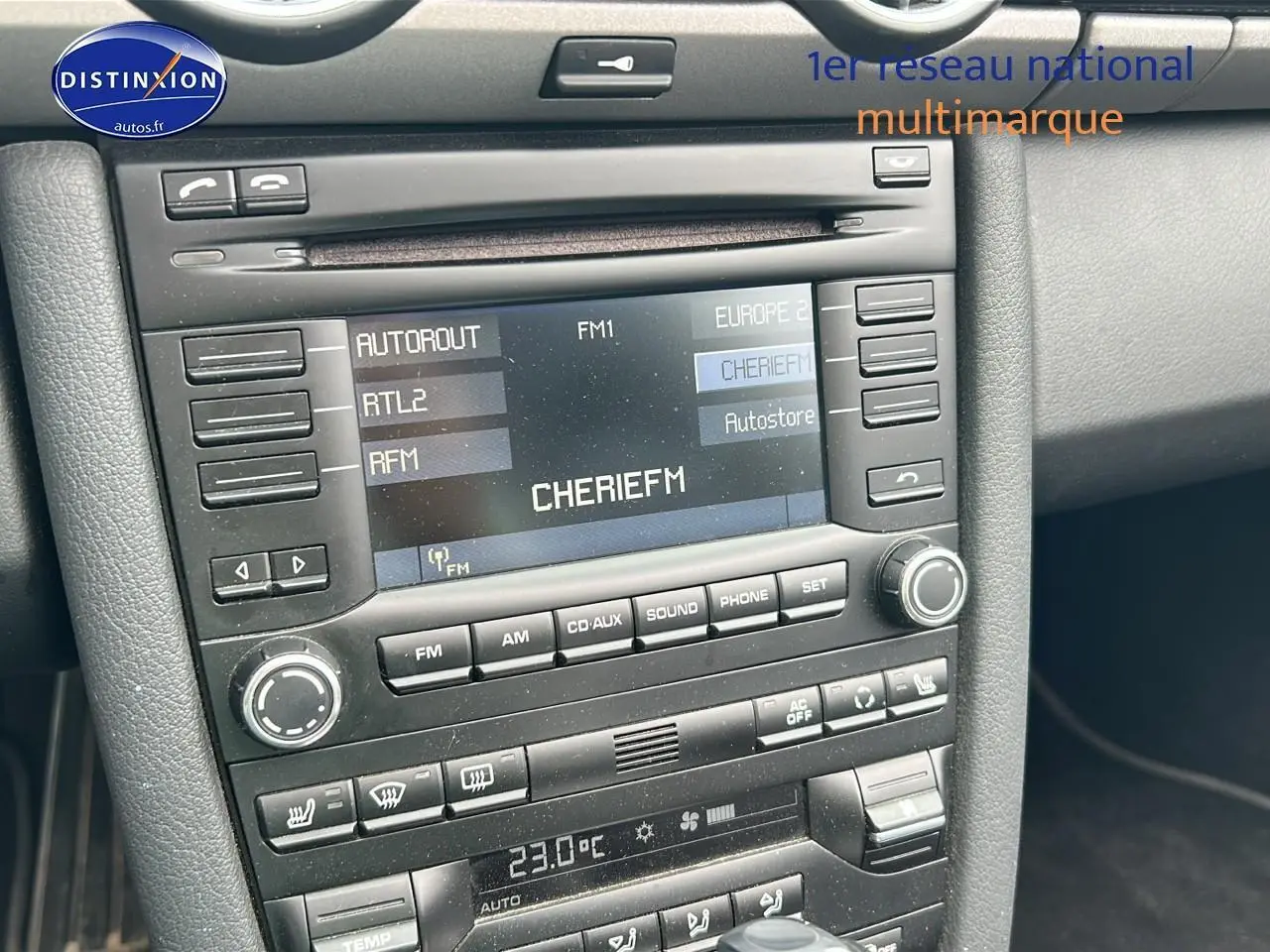 Vue rapprochée du tableau de bord noir de la Porsche Boxster 987 avec écran radio affichant la station CHERIE FM.