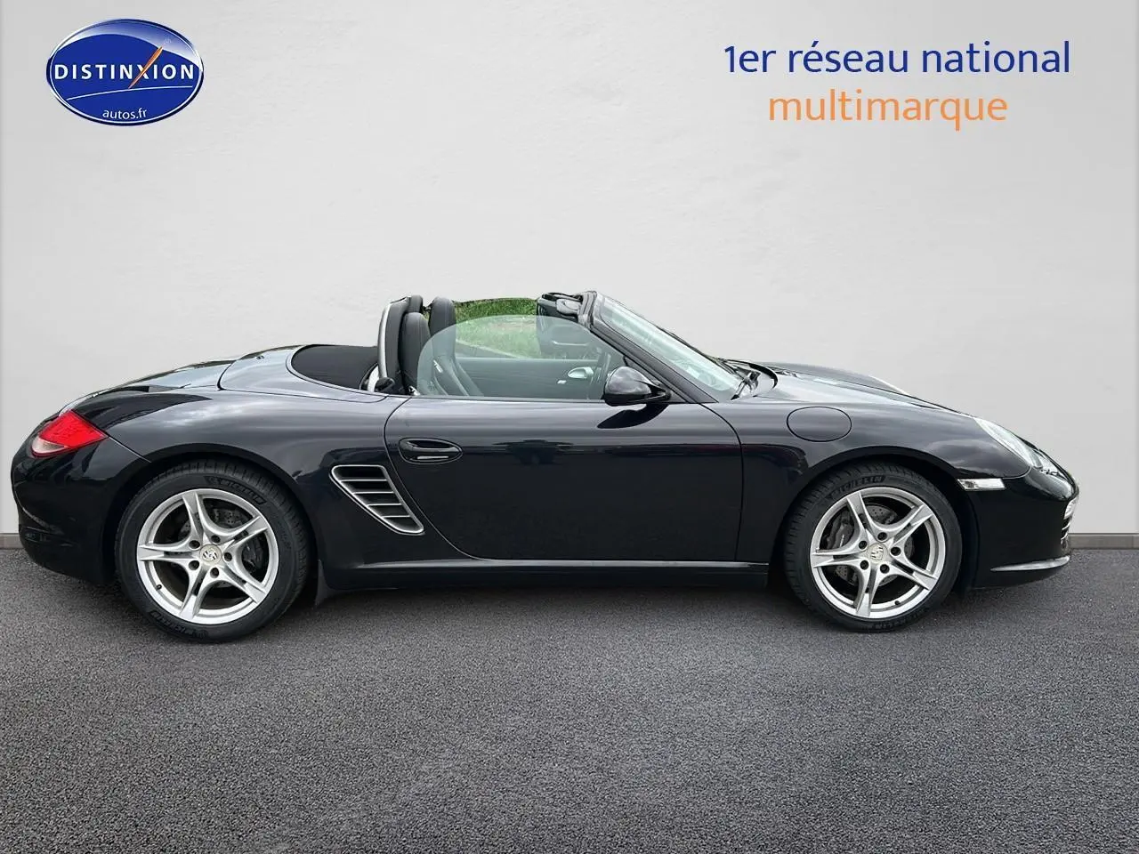 Profil côté gauche d'une Porsche Boxster 987 noire cabriolet, avec jantes alu 17 pouces et capote ouverte.