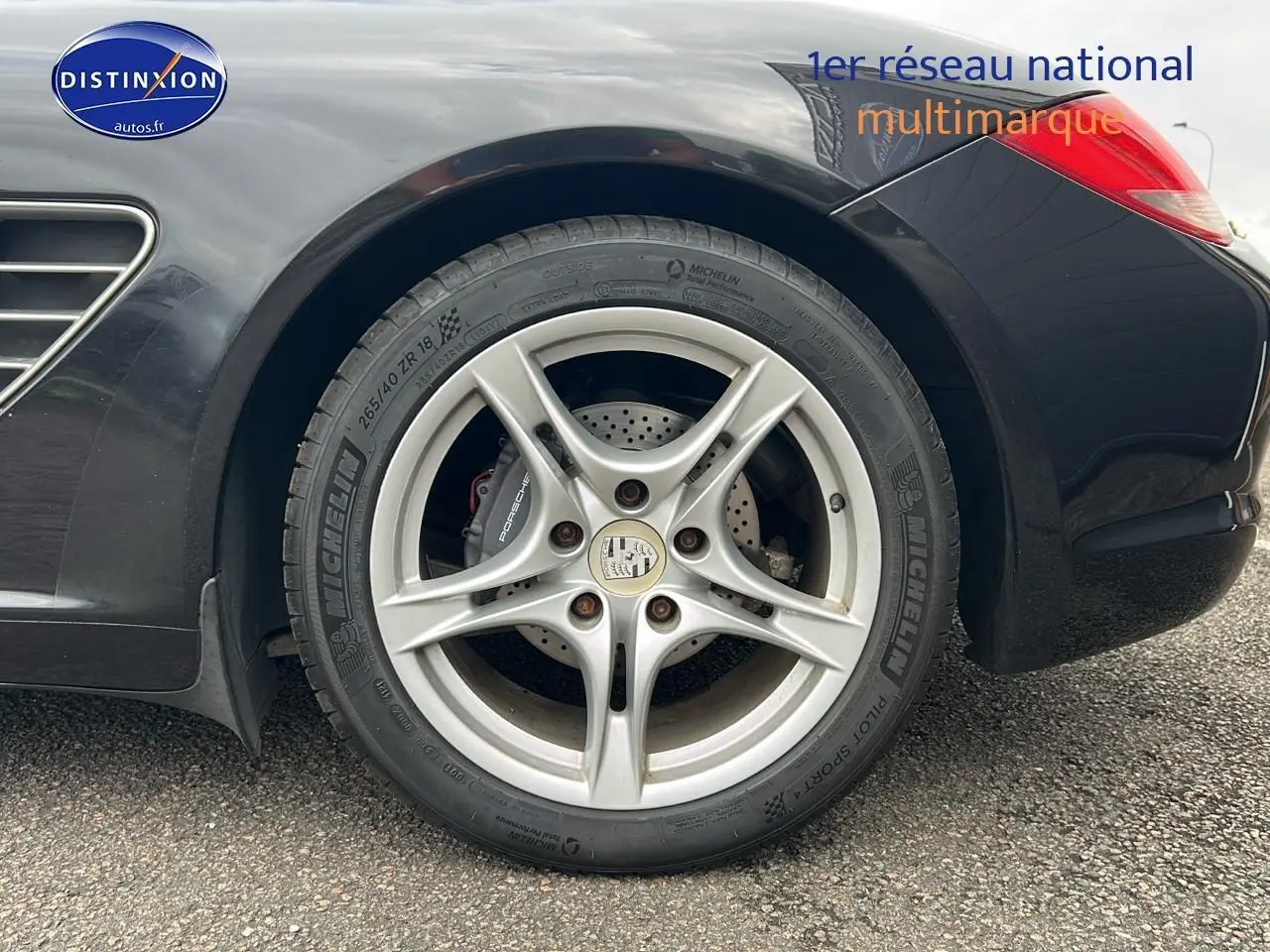 Gros plan sur la jante alu 17 pouces côté arrière droit d'une Porsche Boxster noire avec logo Porsche visible.