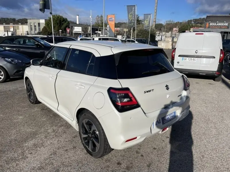 Vue 3/4 arrière droite d'une Suzuki Swift blanche 2025 avec toit noir et feux arrière LED distinctifs.