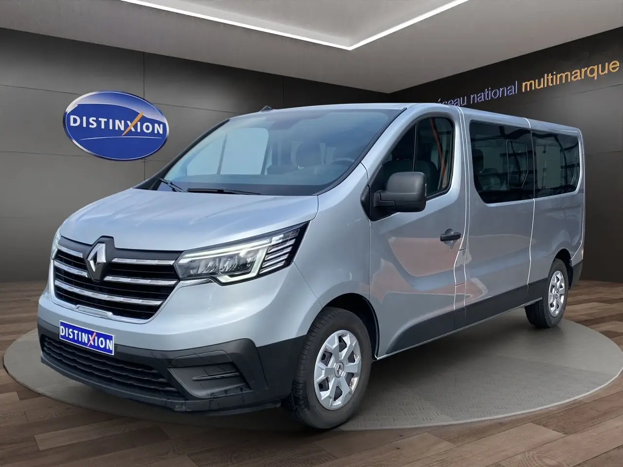Vue 3/4 avant droit d'un Renault Trafic Combi gris platine 2023 avec calandre chromée et vitres teintées.