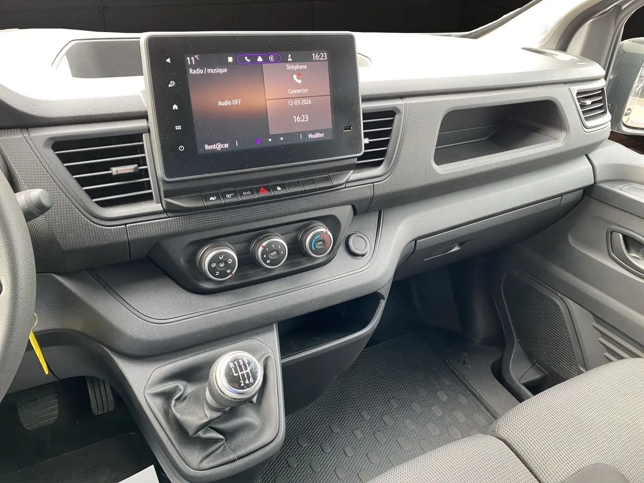 Vue intérieure côté passager du tableau de bord gris et de la console centrale avec écran tactile et levier de vitesses manuel.