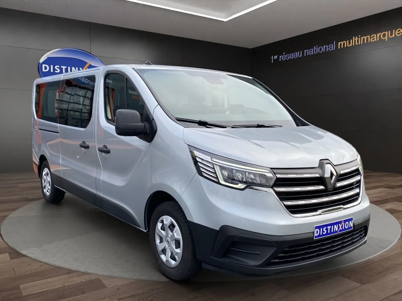 Vue 3/4 avant gauche d’un Renault Trafic Combi gris platine 2023, grand utilitaire neuf avec calandre chromée.