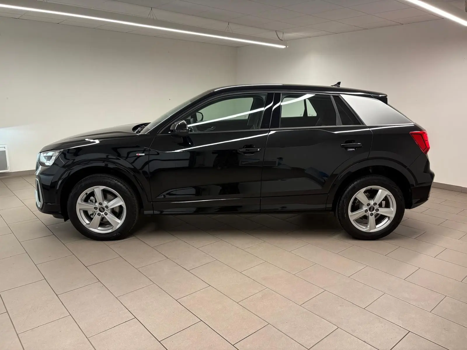 Audi Q2 35 TFSI S Line noir mythic vue de profil côté gauche dans un intérieur neutre, jantes alliage visibles.