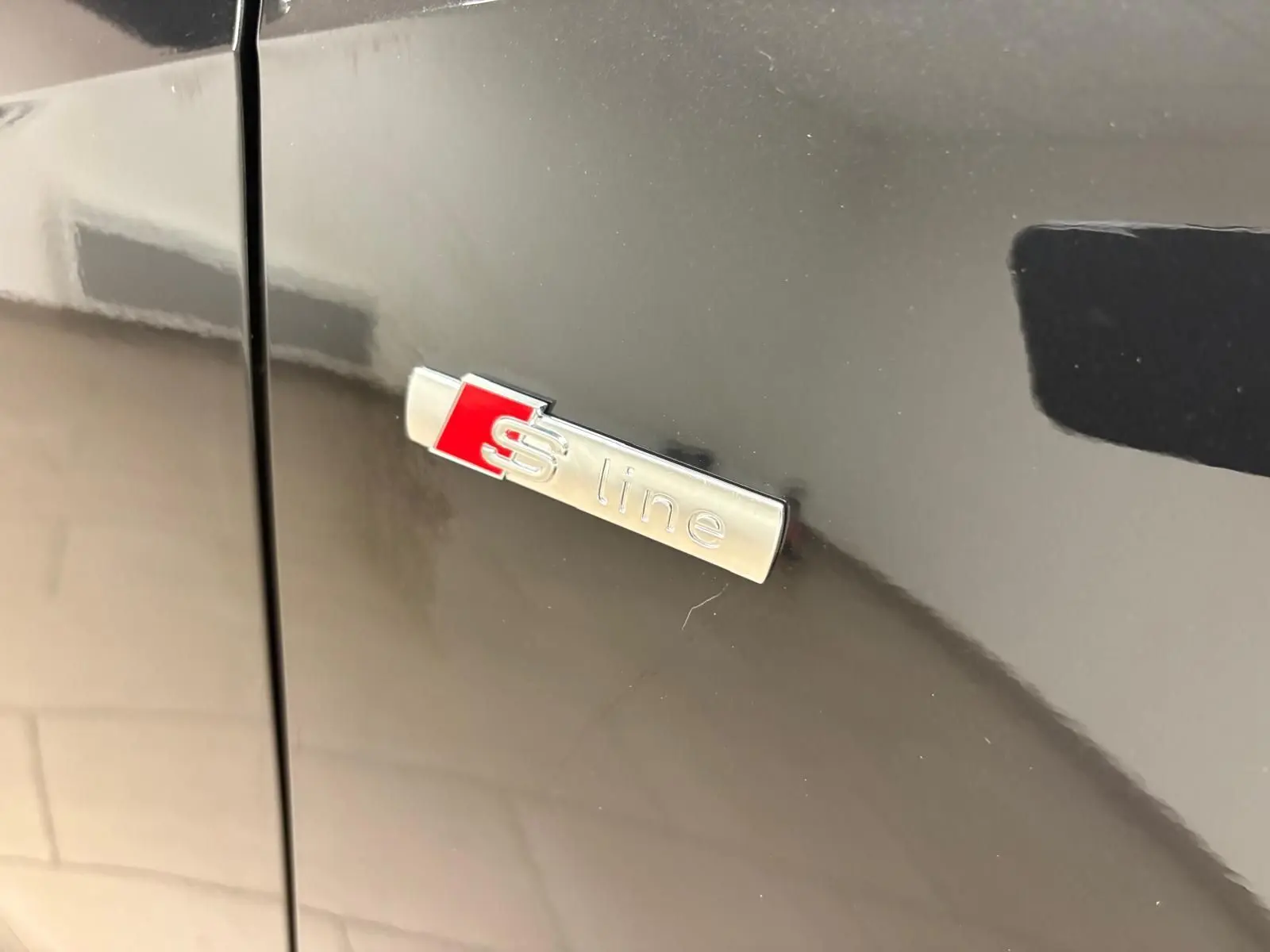 Gros plan sur l'emblème S line argent et rouge sur la porte latérale d'un Audi Q2 noir Mythic.