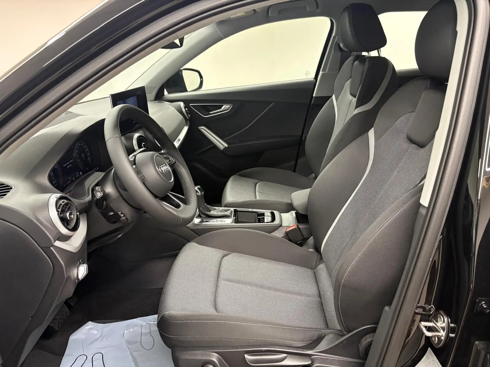 Vue intérieure côté conducteur de l'Audi Q2 35 TFSI S Line 2026 avec sièges tissu gris et tableau de bord noir.