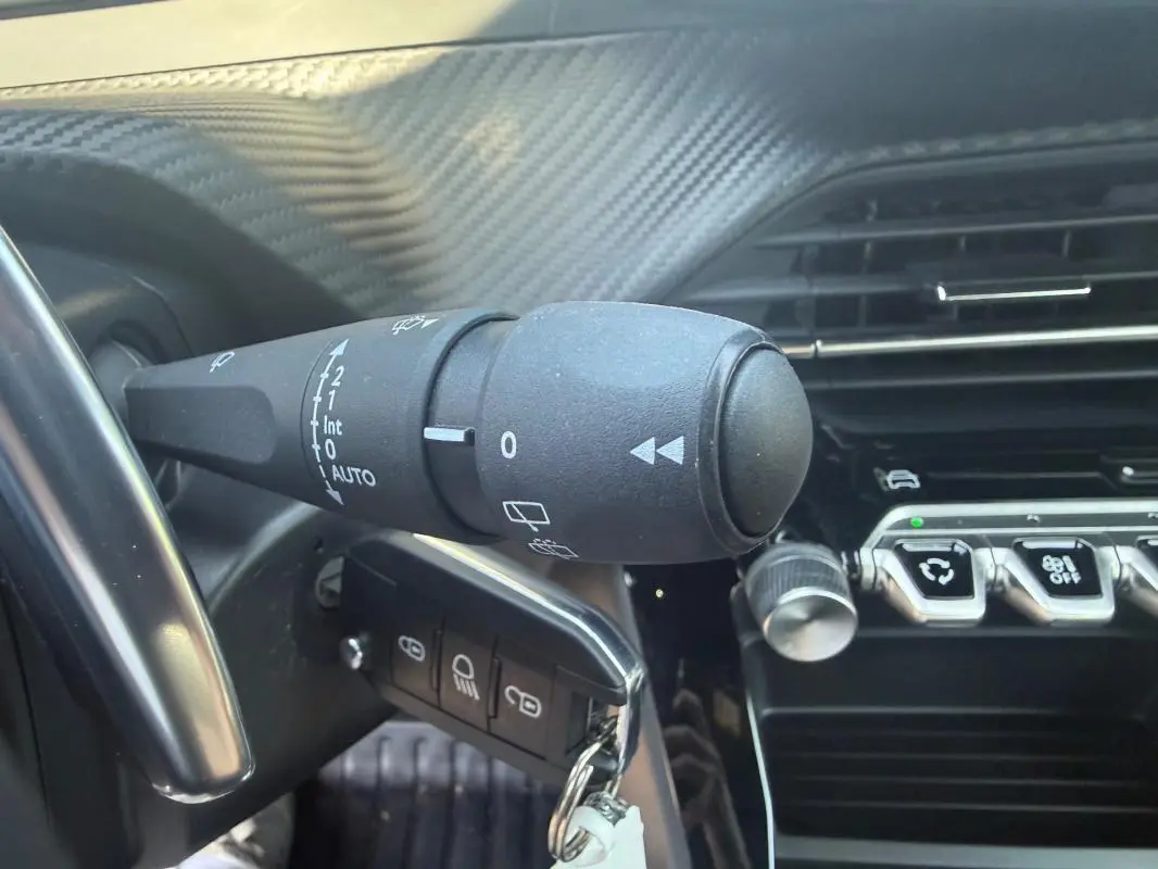 Gros plan sur la commande d’essuie-glace et la clé insérée dans le contacteur du Peugeot 2008 Hybrid noir, intérieur moderne.