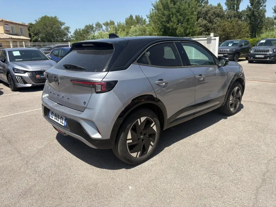 Vue 3/4 arrière droite de l'Opel Mokka électrique gris avec toit noir et jantes alliage 17 pouces sur parking.