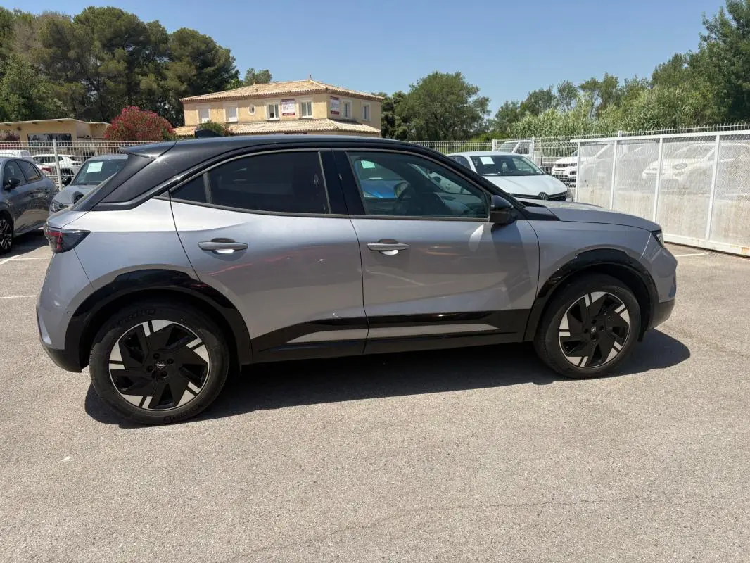 Vue de profil côté gauche d’un Opel Mokka électrique gris avec jantes alliage noires et vitres surteintées.
