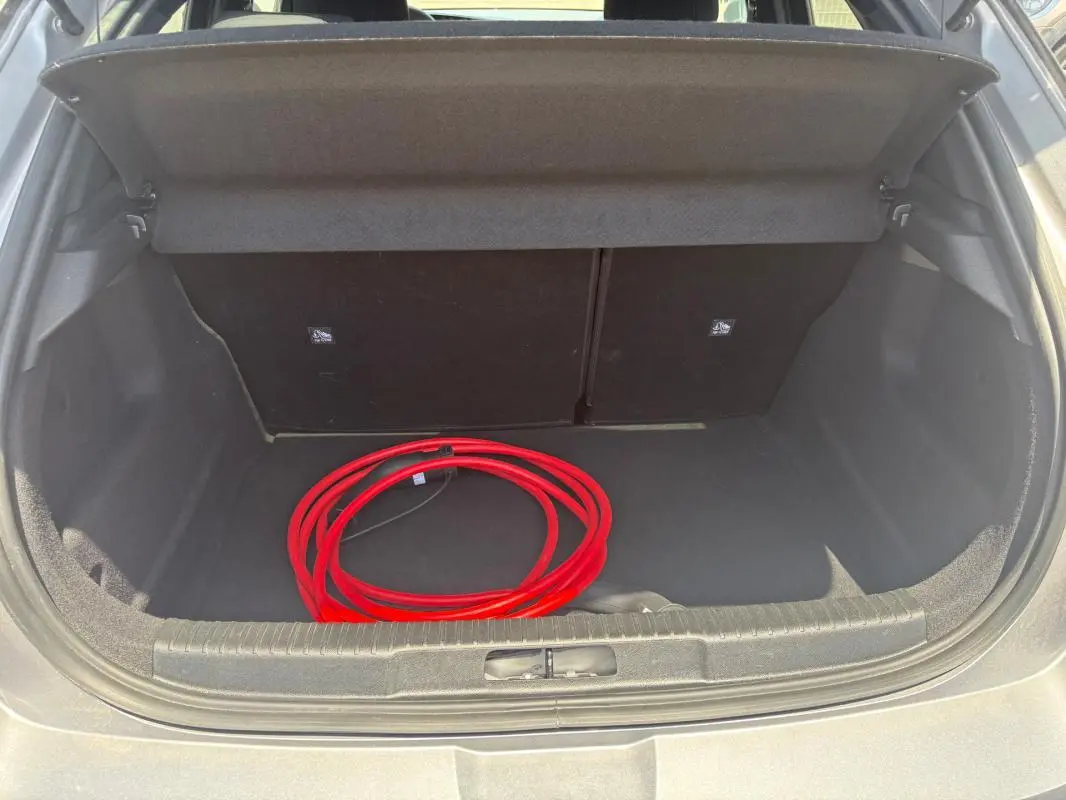 Coffre ouvert d’un Opel Mokka électrique gris, vue arrière, avec câble de recharge rouge visible à l’intérieur.
