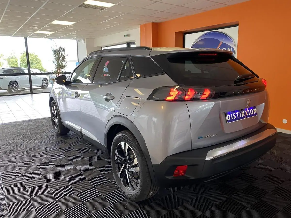 Vue 3/4 arrière droite du Peugeot 2008 e-136 Allure Pack gris Artense avec jantes bi-tons et vitres surteintées en showroom.