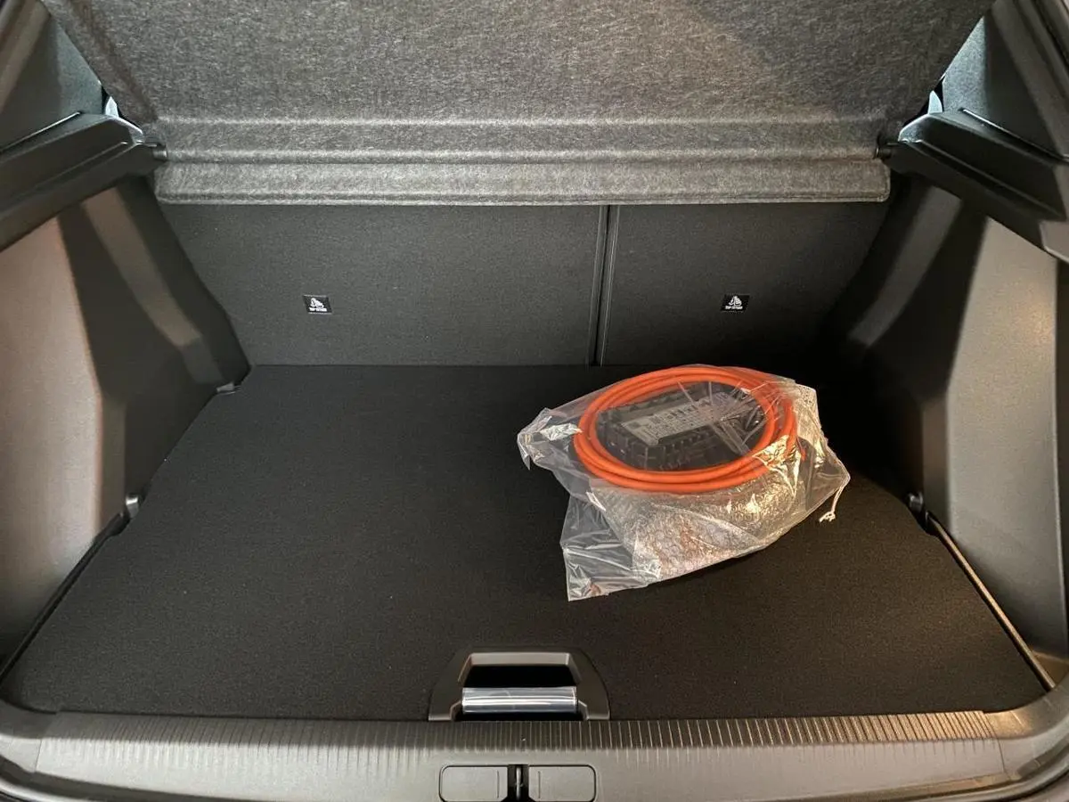 Coffre ouvert d'un Peugeot 2008 e-136 Allure Pack gris Artense avec câble de recharge électrique rangé sur le tapis noir.