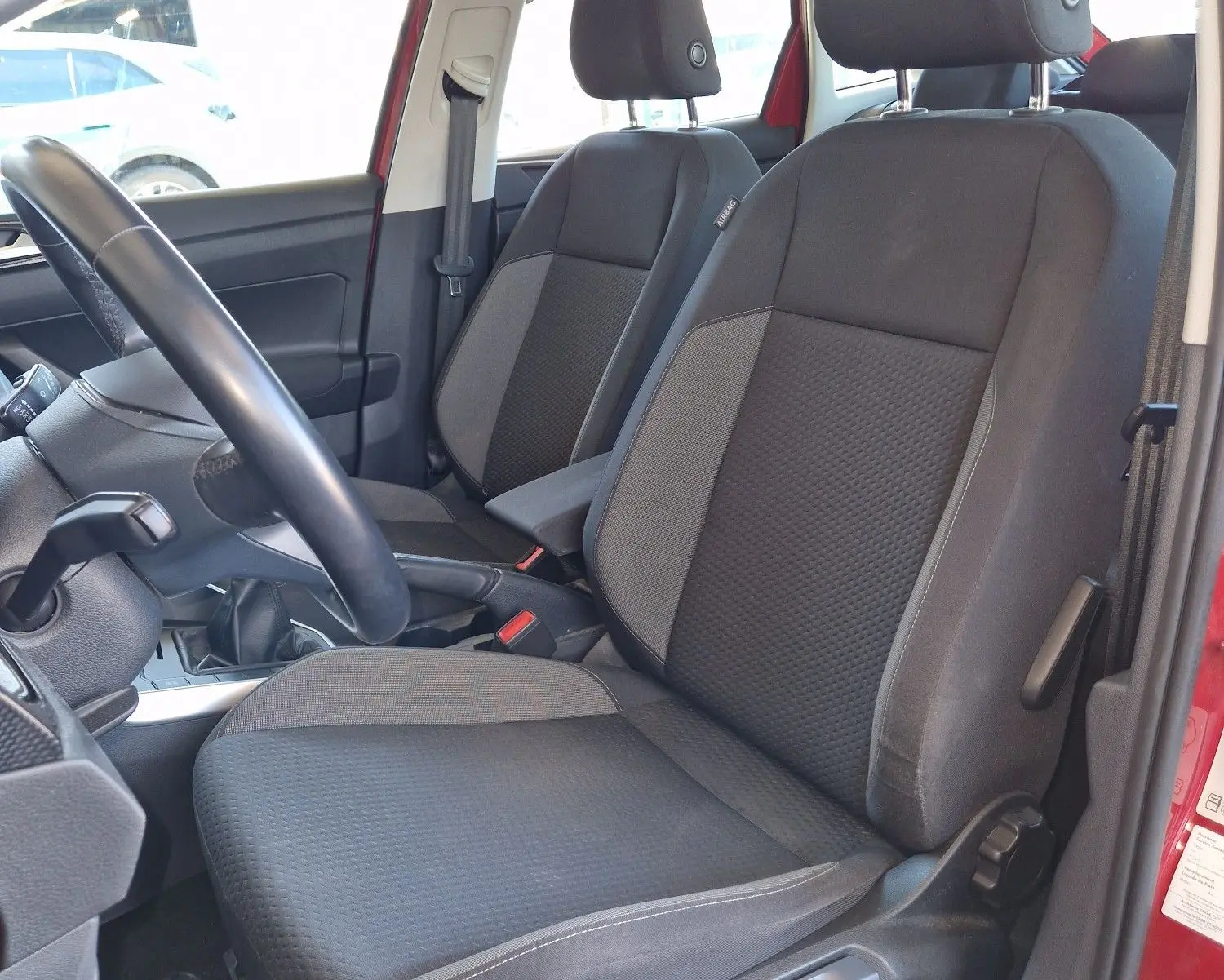 Vue intérieure côté conducteur du Volkswagen Taigo rouge roi 2023, sièges noirs en tissu et volant visible.