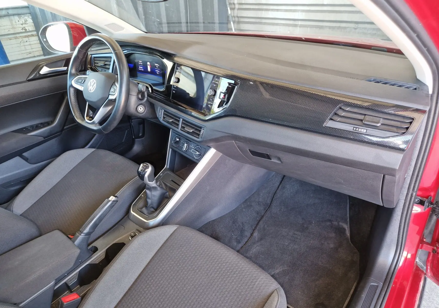 Intérieur côté conducteur du Volkswagen Taigo rouge roi 2023, avec tableau de bord moderne et boîte manuelle visible.