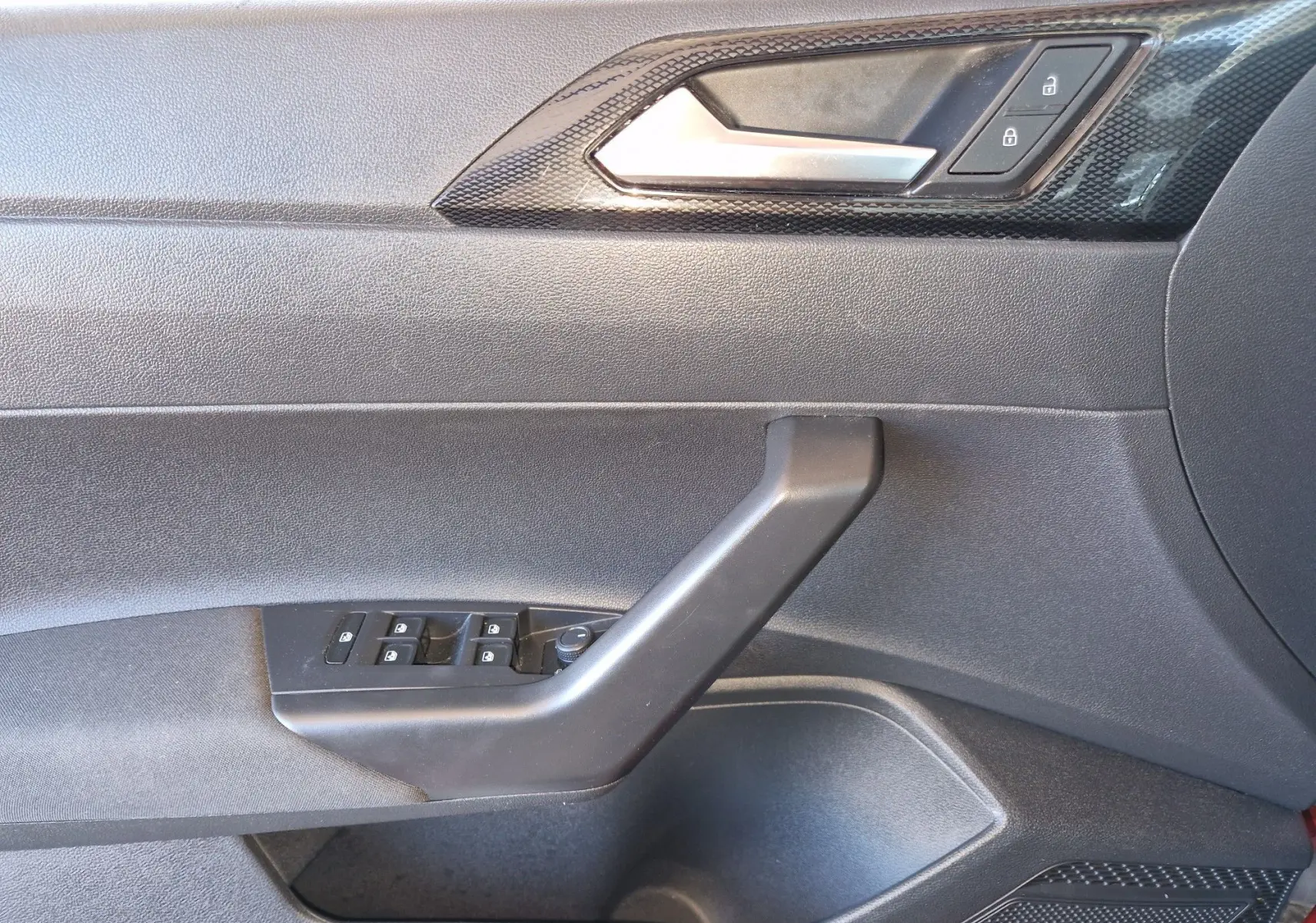 Vue intérieure côté conducteur de la porte d'une Volkswagen Taigo rouge roi 2023 avec commandes de vitres et verrouillage.
