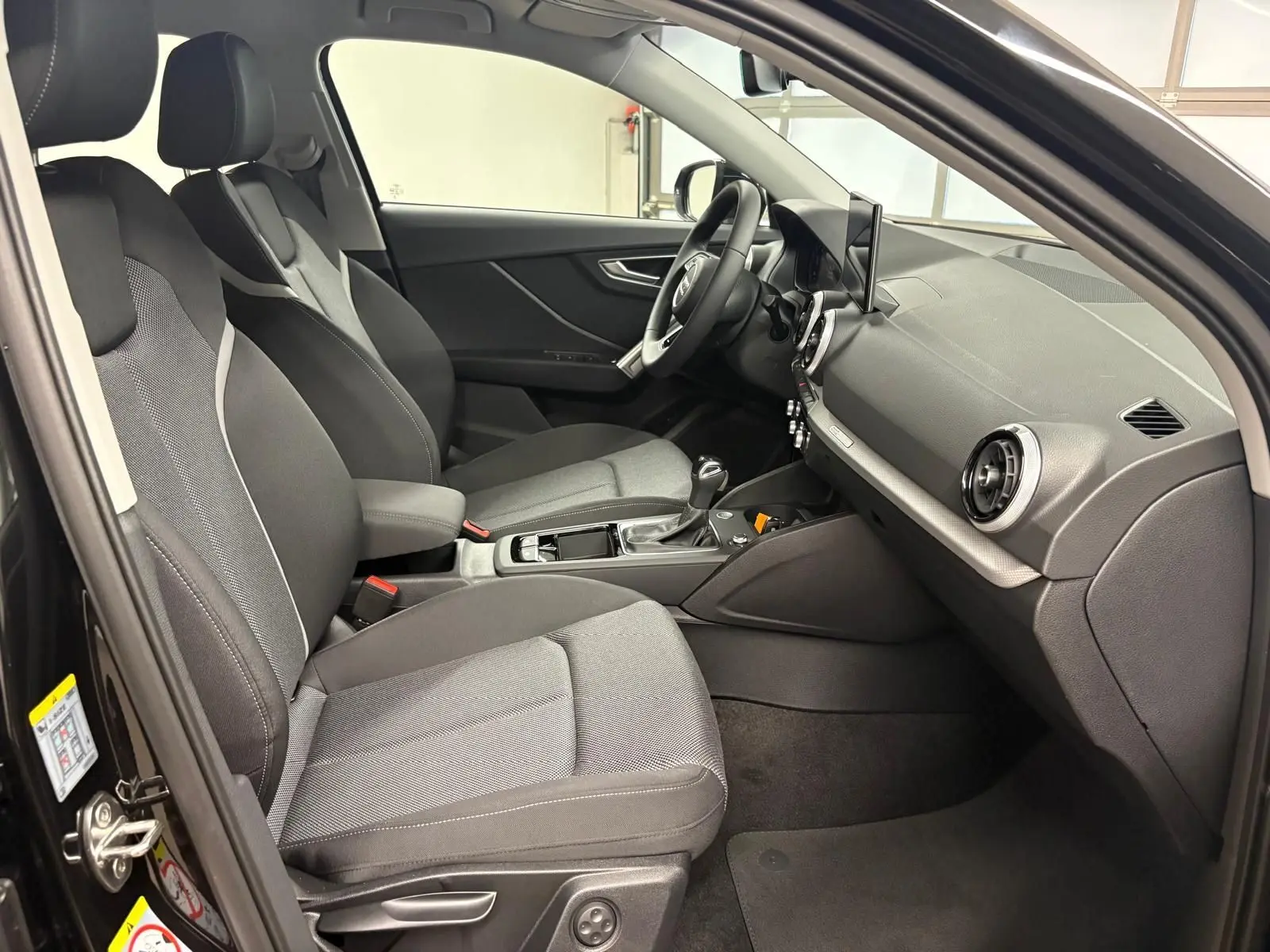Vue intérieure côté conducteur de l'Audi Q2 35 TFSI S Line 2026 avec sièges tissu gris et tableau de bord noir.
