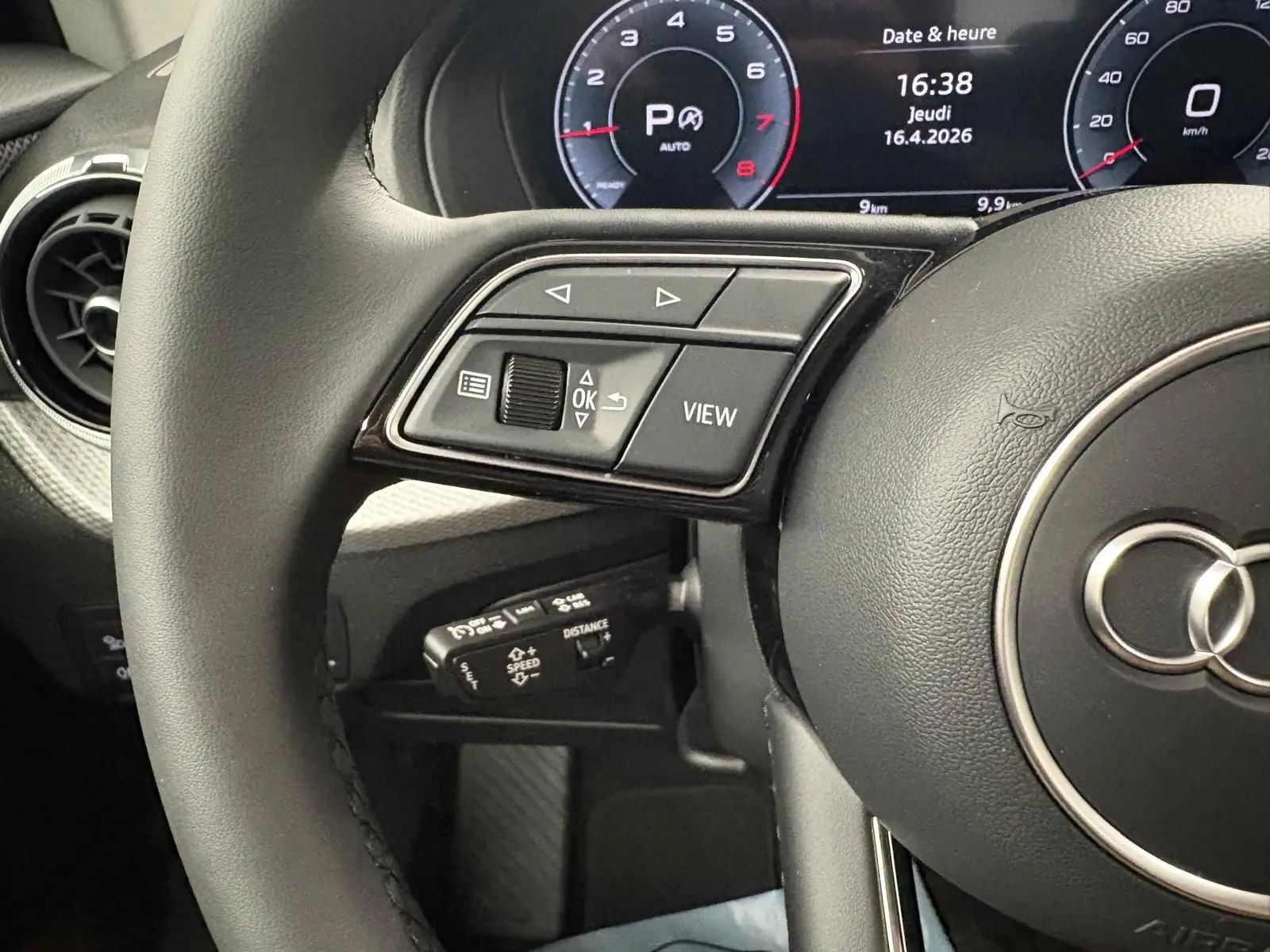 Gros plan sur le volant noir et le tableau de bord digital de l'Audi Q2 35 TFSI S Line 2026, affichant date et heure.