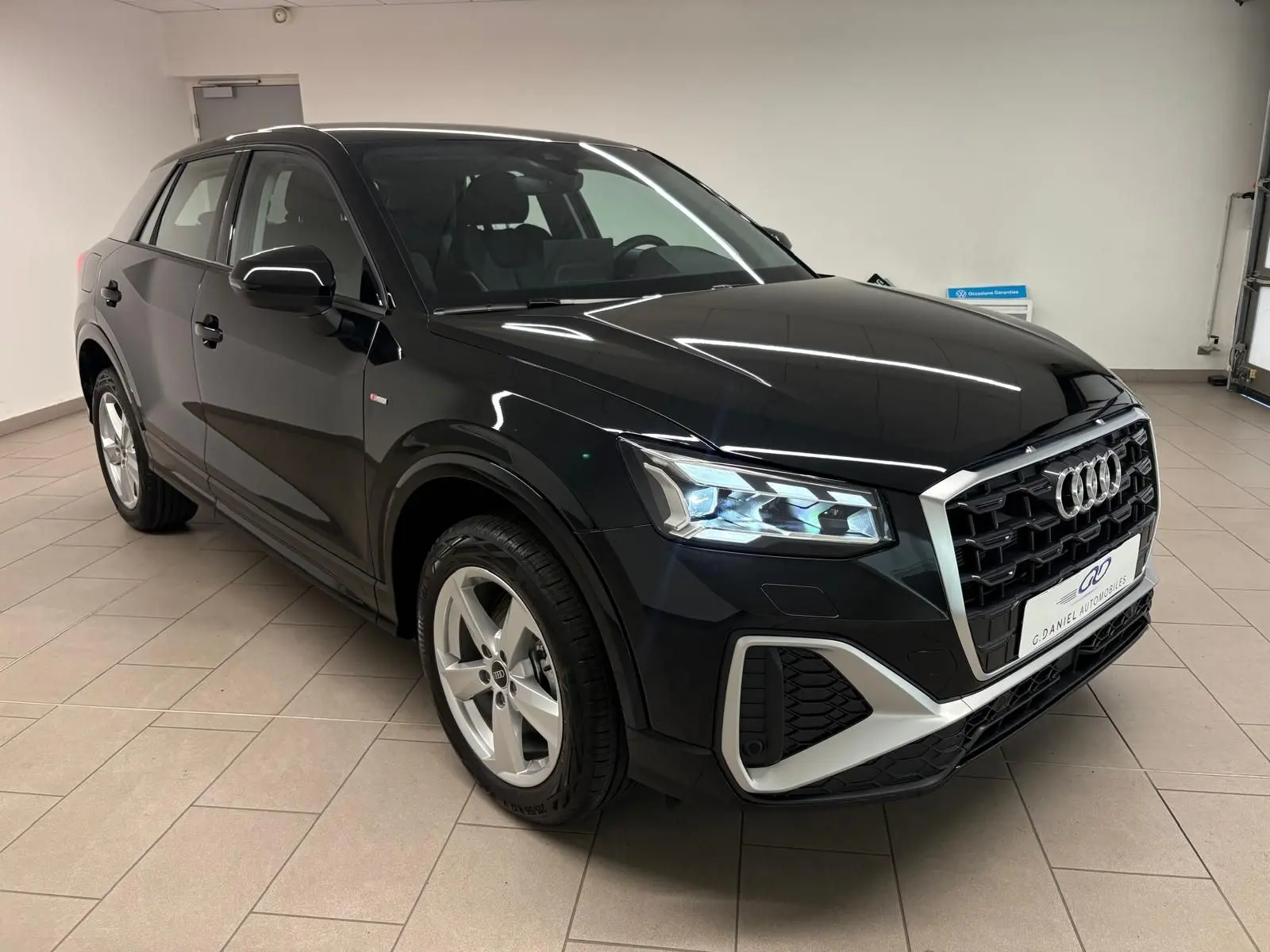 Audi Q2 35 TFSI S Line noir mythic en 3/4 avant droit, avec calandre hexagonale et phares LED allumés.