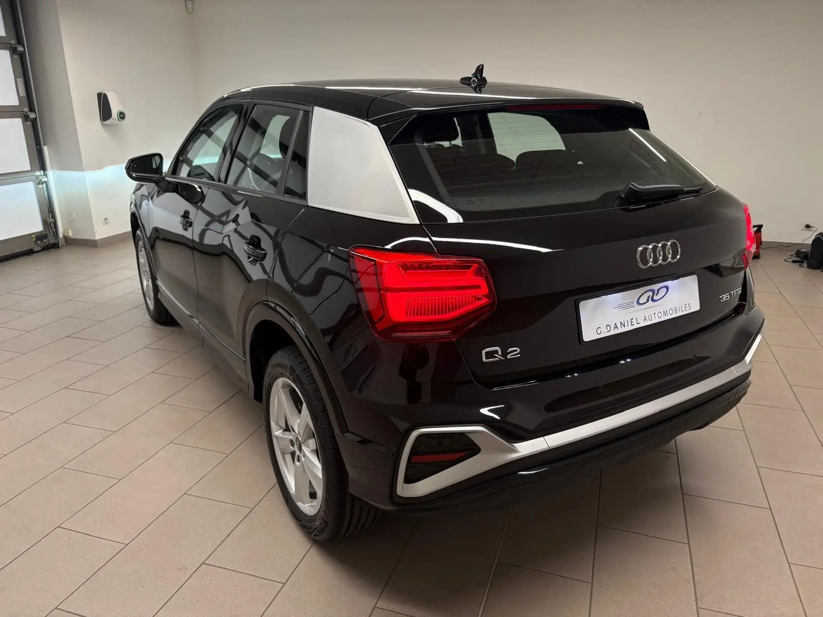 Vue 3/4 arrière droite d'un Audi Q2 35 TFSI S Line noir Mythic avec toit contrastant et feux arrière allumés.