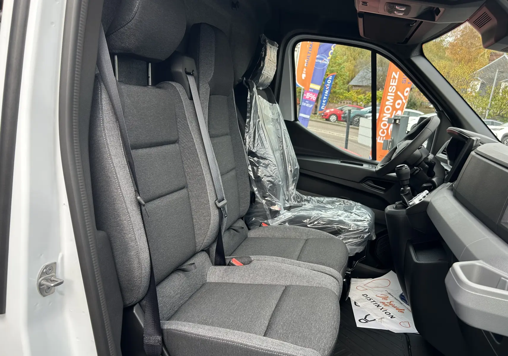 Vue intérieure côté conducteur du Renault Master blanc 2025, montrant les sièges avant en tissu gris et le volant.
