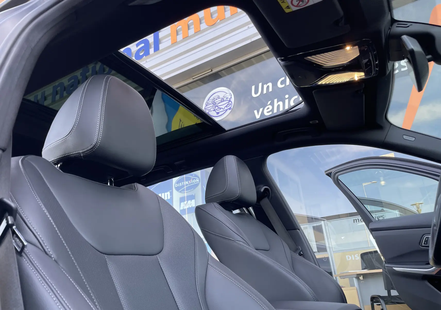 Intérieur noir cuir de la BMW Série 3 Touring G21 2022, vue côté gauche avec toit panoramique ouvert et porte avant ouverte.