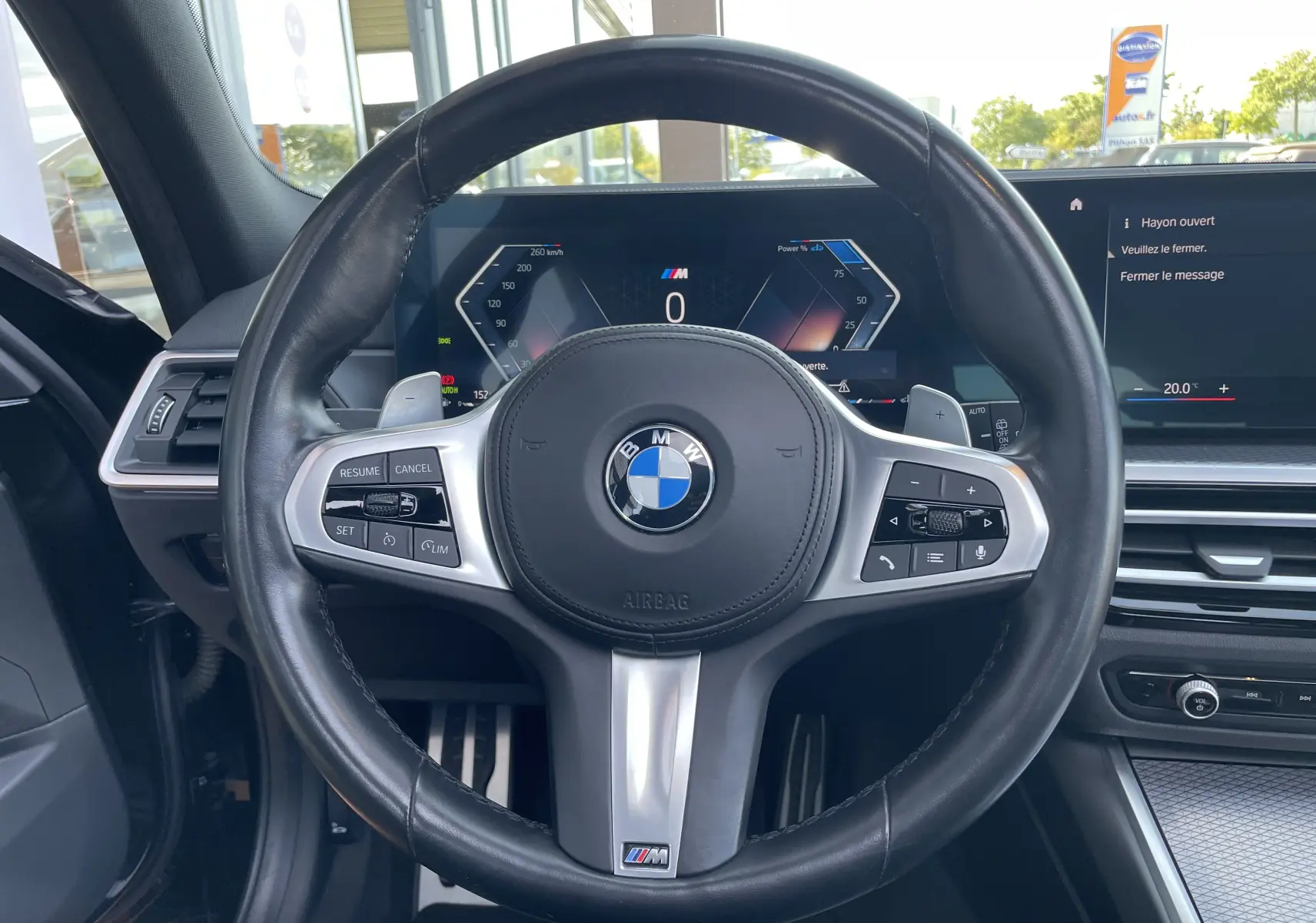 Vue rapprochée du volant cuir noir M Sport de la BMW Série 3 Touring G21 avec tableau de bord numérique allumé.