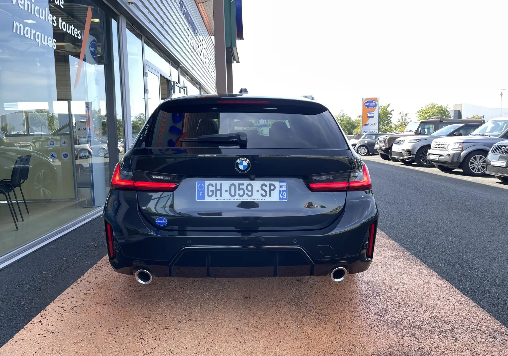 Vue arrière d'une BMW Série 3 Touring G21 noire métal avec feux LED allumés et double sortie d'échappement chrome.