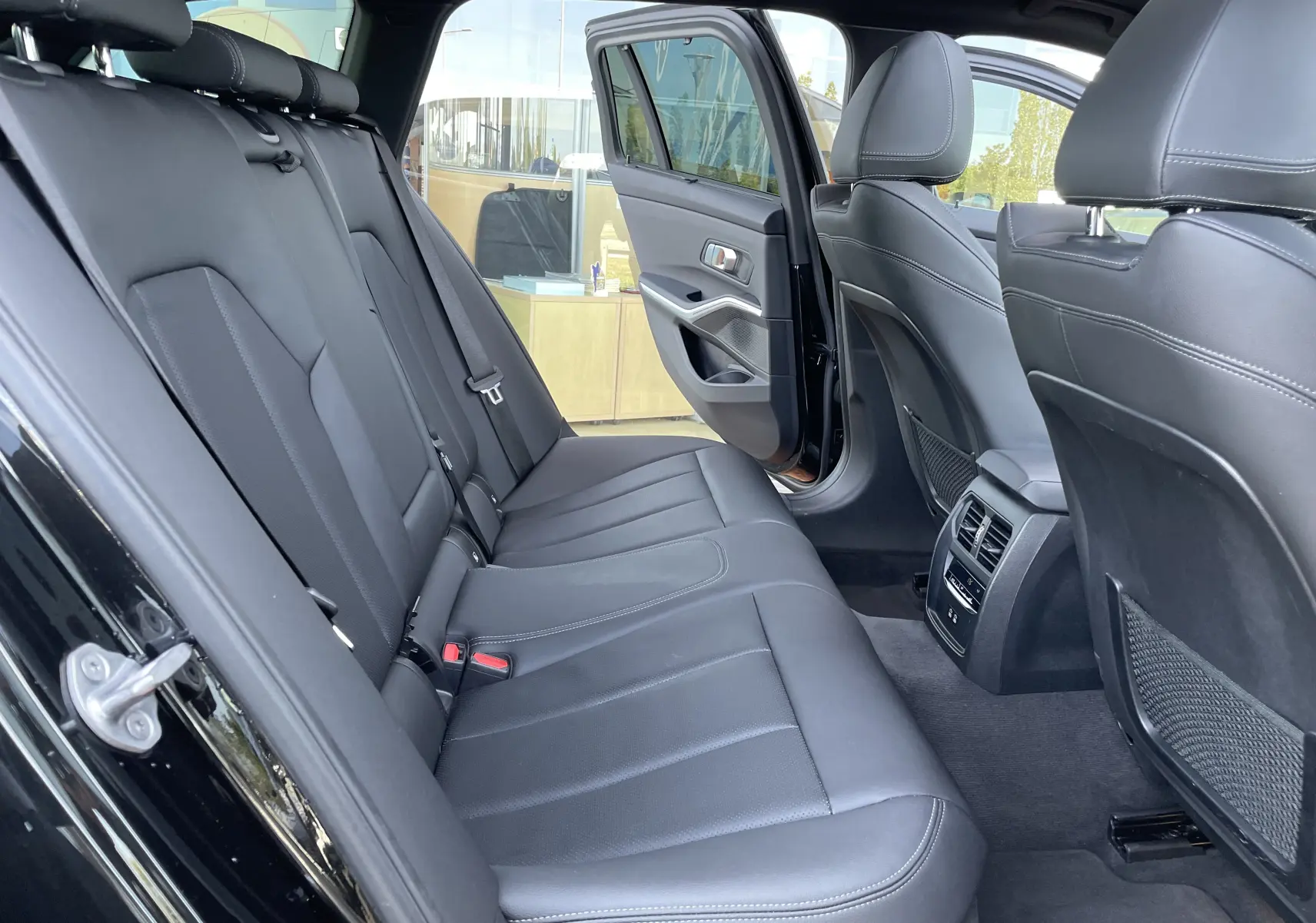 Vue intérieure arrière côté gauche d'une BMW Série 3 Touring G21 noire, montrant les sièges en cuir noir et la portière ouverte.