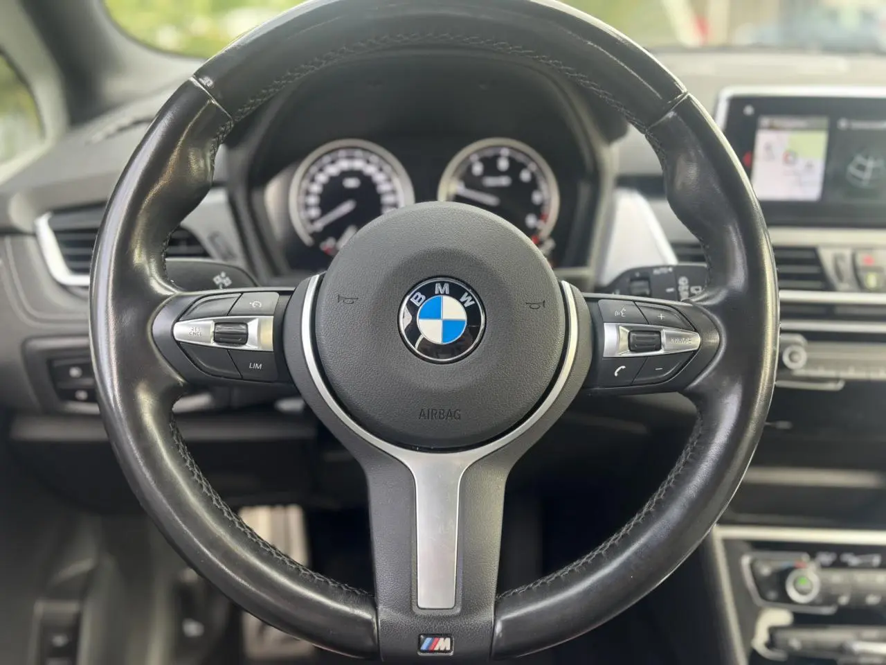 Vue rapprochée du volant cuir M noir de la BMW Série 2 Active Tourer 218dA 2020 avec tableau de bord et écran GPS en arrière-plan.