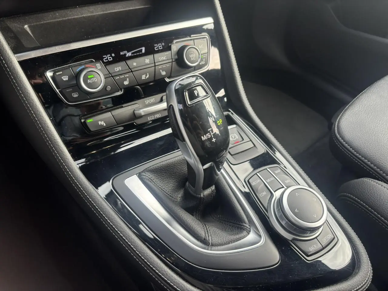 Gros plan sur la console centrale noire de la BMW Série 2 Active Tourer blanche, avec levier de vitesse automatique et commandes multimédia.