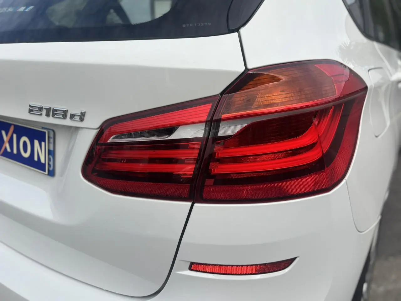 Gros plan sur le feu arrière droit d’une BMW Série 2 Active Tourer 218d blanche, avec badge moteur visible.