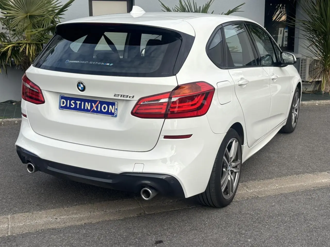 BMW Série 2 Active Tourer 218d blanc vue 3/4 arrière droit avec jantes alliage 18 pouces et double sortie d’échappement.