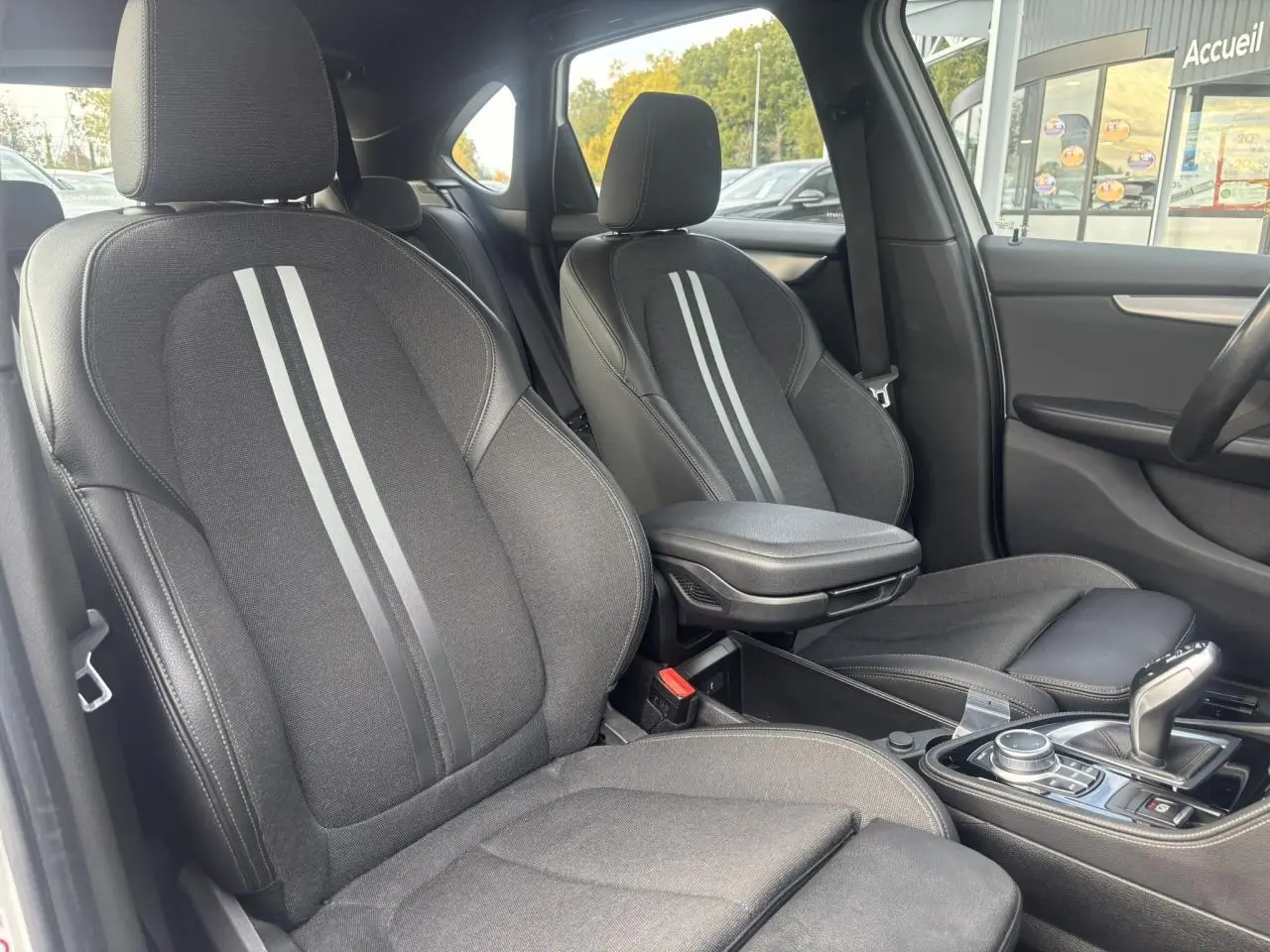 Vue intérieure côté avant droit de la BMW Série 2 Active Tourer 218dA M Sport, sièges noirs avec bandes grises et accoudoir central.