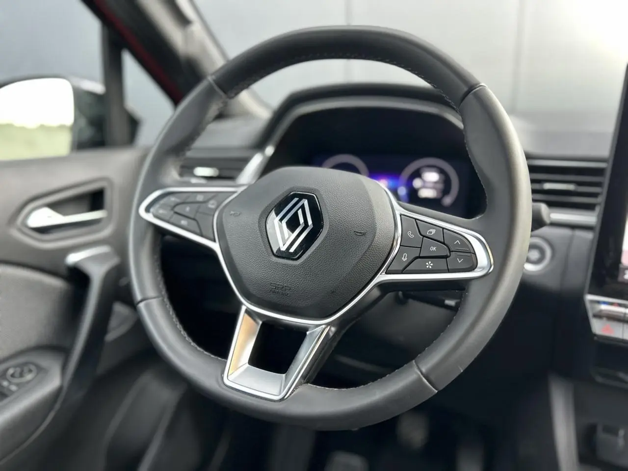 Vue rapprochée du volant noir du Renault Captur 2025 avec commandes intégrées et tableau de bord numérique flou en arrière-plan.