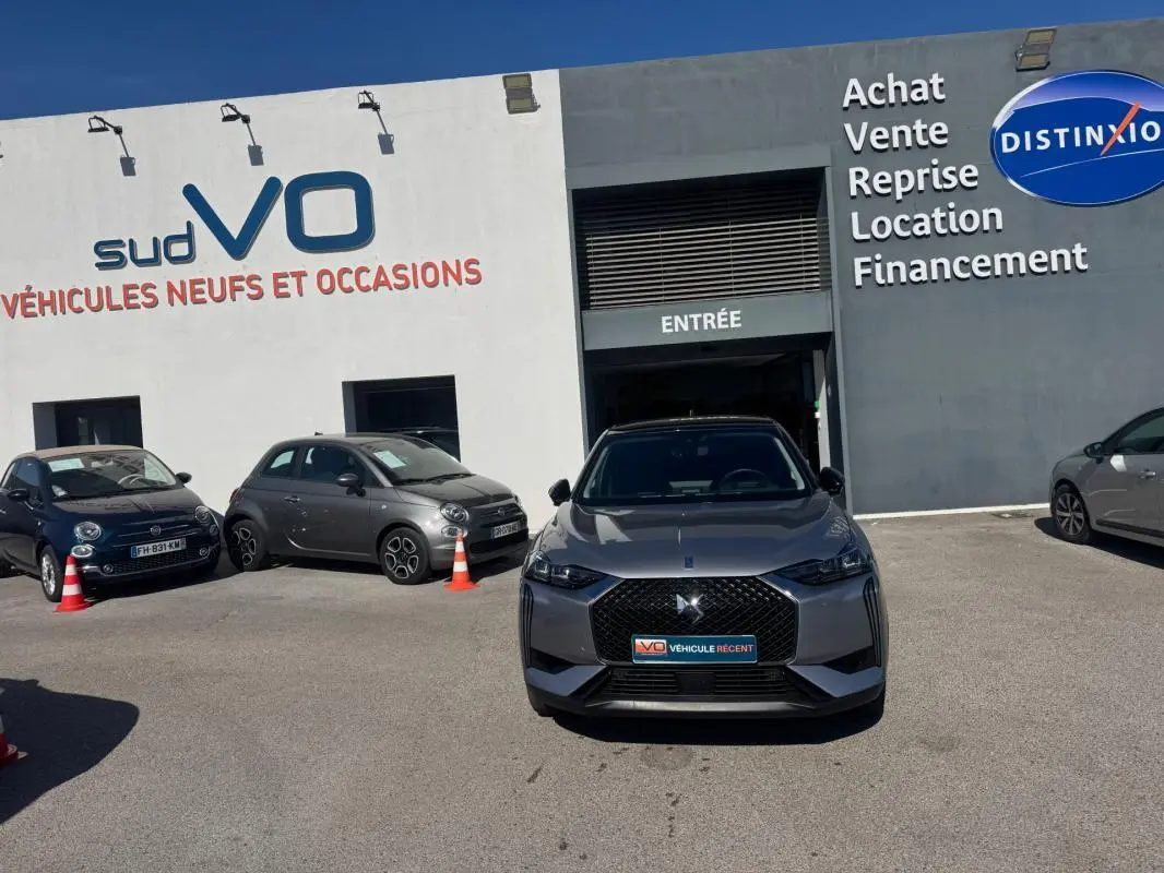 Vue avant d'une DS3 100 BVM6 Bastille gris 2024 avec calandre noire et jantes alliage 18 pouces, stationnée devant un garage.