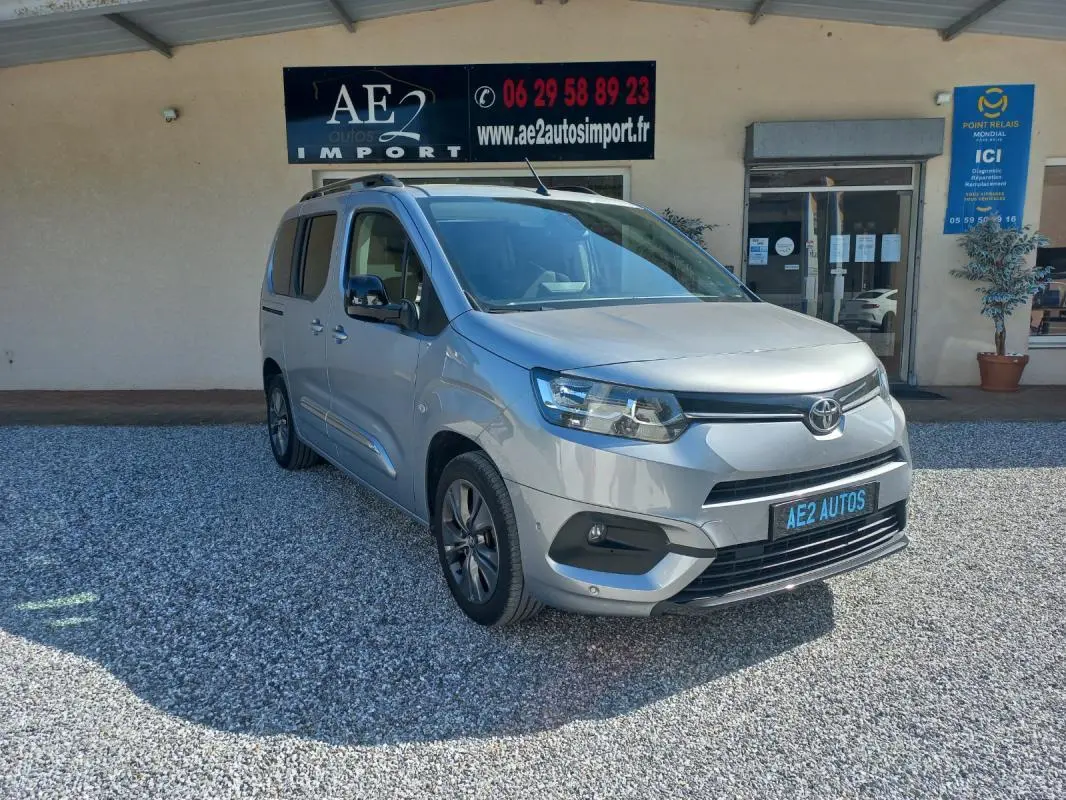 Toyota Proace City Verso gris vue 3/4 avant droit, avec calandre noire et jantes alliage, stationné devant un bâtiment.