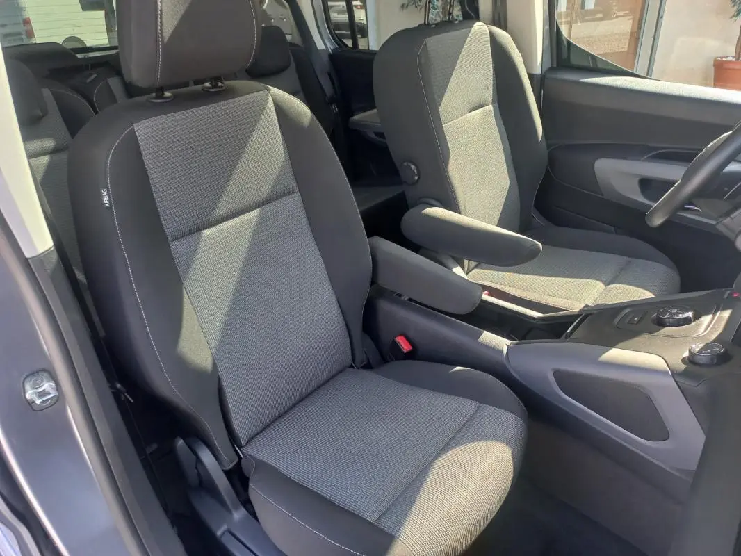 Vue intérieure côté conducteur du Toyota Proace City Verso gris 2023, sièges tissu avec accoudoirs et console centrale visible.
