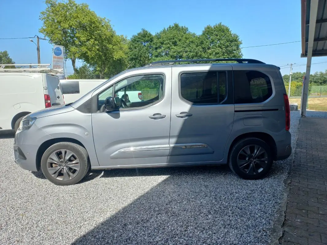 Vue de profil côté gauche d’un Toyota Proace City Verso gris 2023 garé sur un sol gravillonné, avec jantes foncées.