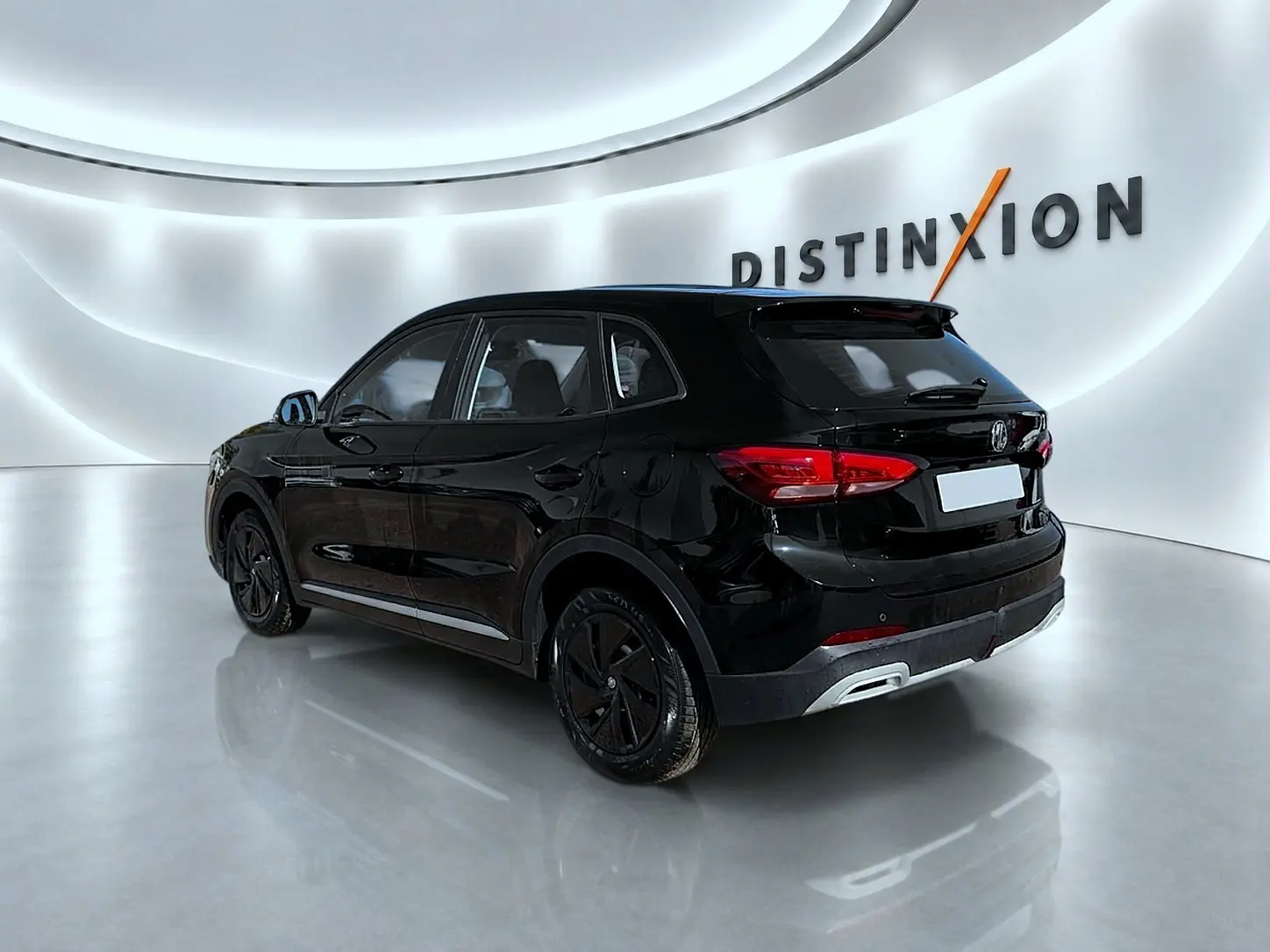 Vue 3/4 arrière droite d'un MG ZS noir brillant dans un showroom lumineux avec logo Distinxion en arrière-plan.
