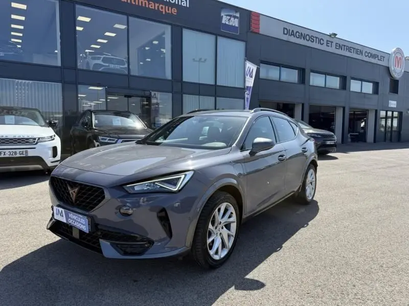 Vue 3/4 avant droite d'un CUPRA Formentor gris 2023 avec jantes argentées, devant un garage de diagnostic auto.