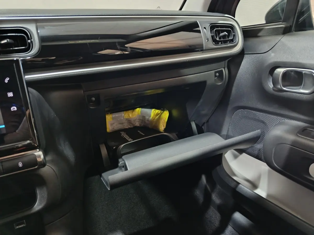 Intérieur de la Citroën C3 2024 gris foncé, vue côté passager avec boîte à gants ouverte et tableau de bord noir brillant.