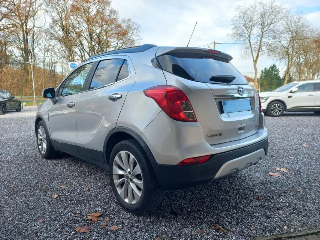 Opel Mokka X gris vue 3/4 arrière côté gauche, avec feux arrière rouges et jantes alliage visibles.