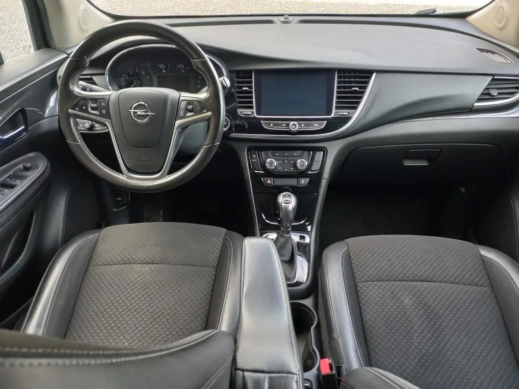 Vue intérieure avant de l'Opel Mokka X 2017, montrant le volant, tableau de bord et sièges noirs en tissu et cuir.